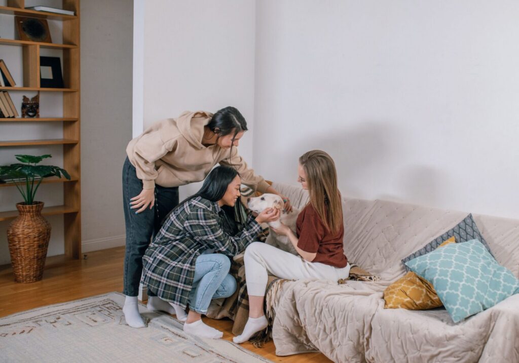 Three friends enjoying a relaxed moment with a dog on a couch, showcasing pet companionship.